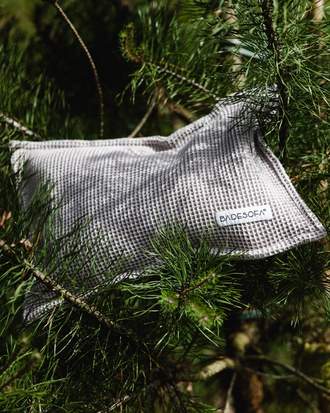 Kopfkissen für die Sauna mit Füllung aus Zirbenspänen liegt in den Ästen einer Zirbenkiefer. In der Farbe Taupe.