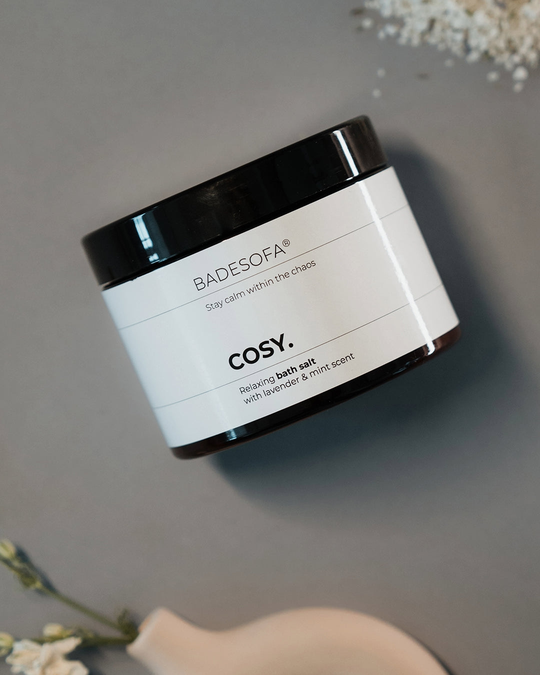 Ein Tiegel mit Badesofa Badesalz liegt dekoriert zwischen Salz und Blumen.