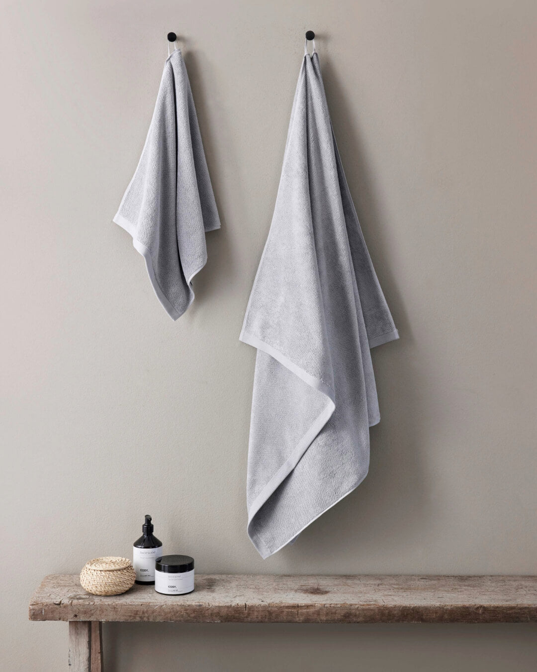 Ein Handtuch und ein Badetuch hängen an Haken an der Wand, Farbe Grau 