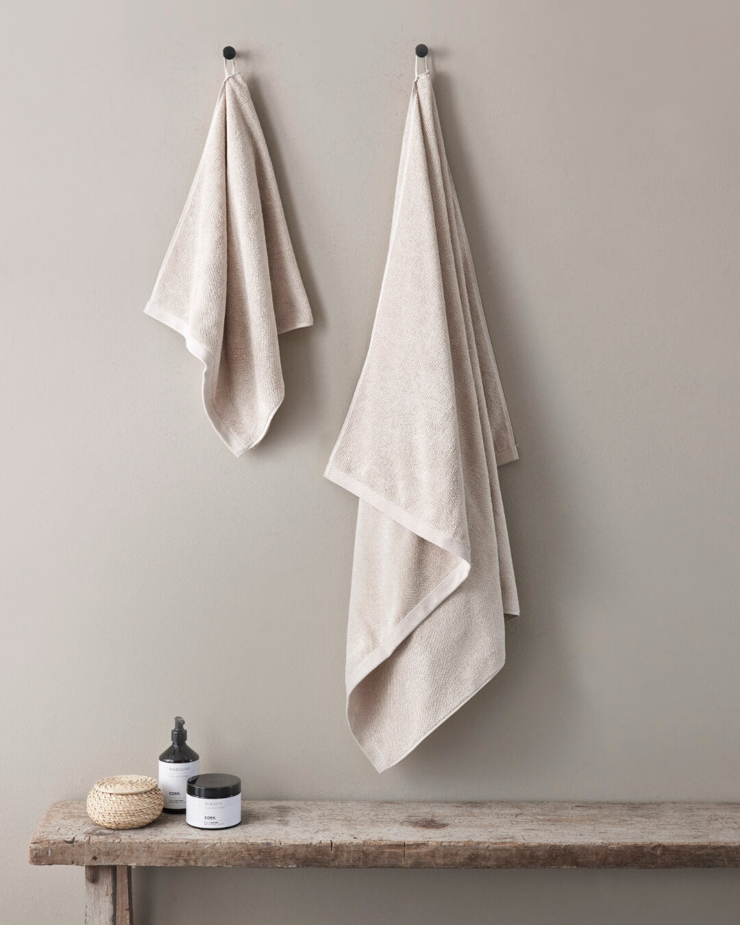 Ein Handtuch und ein Badetuch hängen an Haken an der Wand, Farbe Nature. 