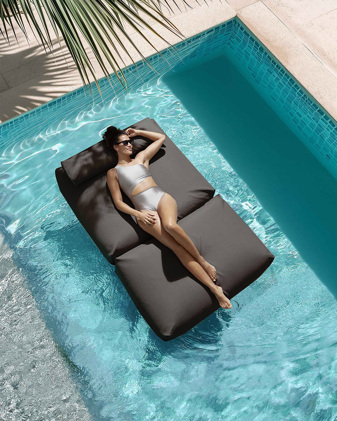 Eine Frau liegt entspannt auf einem Poolsofa double, das im Pool schwimmt. 