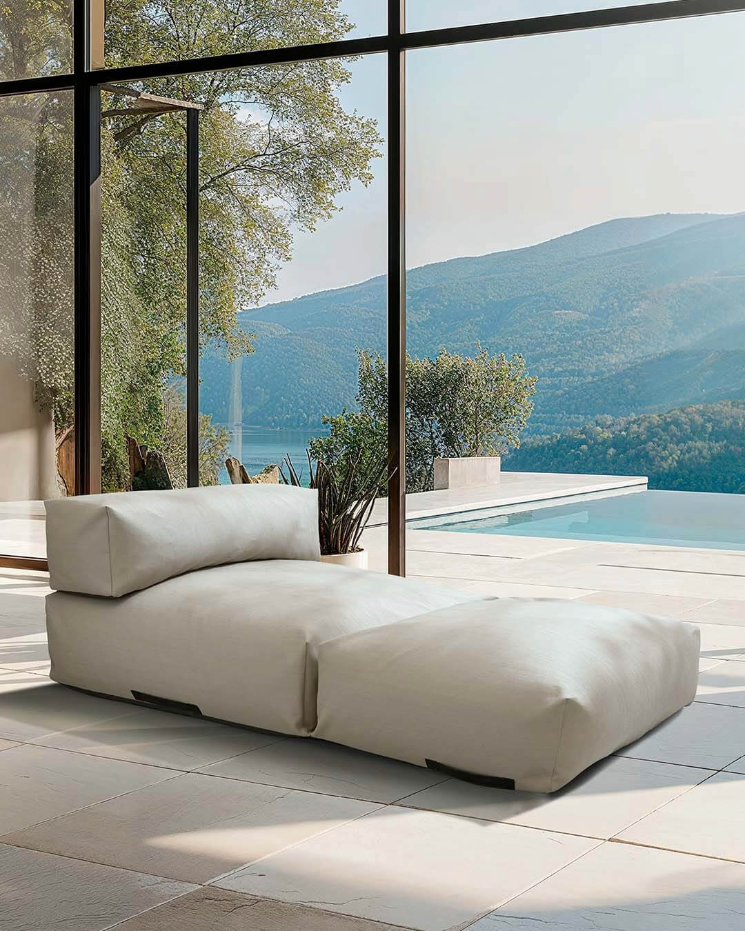 Ein Poolsofa Double in Beige steht in einem Wohnzimmer, die Terrassentür steht offen und der Blick geht auf eine Terrasse mit Pool. $ Poolsofa Double | Beige