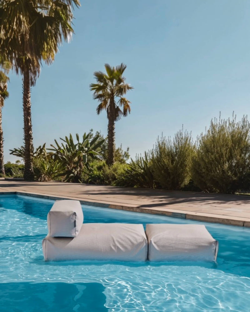 Ein Poolsofa Singel in Beige schwimmt auf dem Pool. Es liegt auf der Waseroberfläche aucf. 