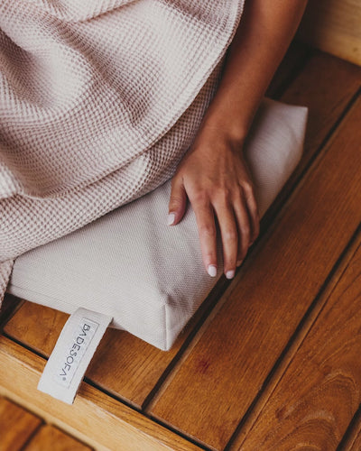 Das Video zeigt eine Frau, die in ein Saunatuch gewickelt auf dem Badesofa Sitzkissen in der Sauna sitzt. 